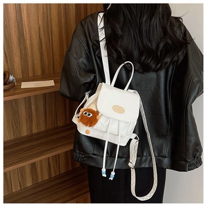 Rear view of a white PU leather mini backpack featuring a plush charm on a wooden background