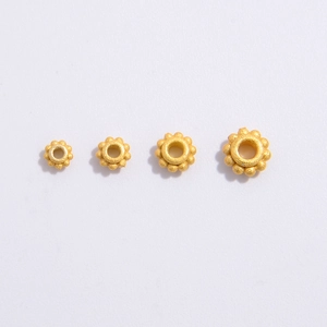 Macro detail of four sizes of gold-toned flower spacers with a matte frosted finish