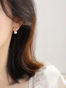 Detail of gold twisted knot earrings featuring an elegant white drop pearl charm