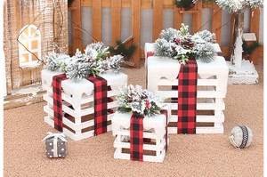 Close-up of white wooden Christmas gift boxes with buffalo plaid bows and snowy accents