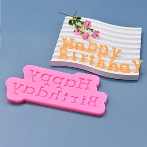 Pink silicone Happy Birthday cake mold with orange fondant letters on a blue surface