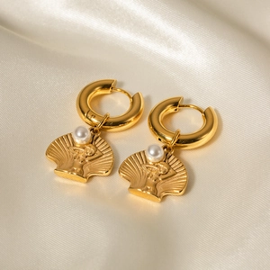 Close-up of golden shell earring with pearl and female figure relief on white silk