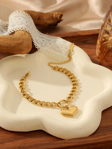 Detailed macro of gold-plated chain bracelet with heart charm on white ceramic tray