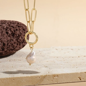 Close-up of gold paperclip link necklace with a pinkish baroque pearl on stone