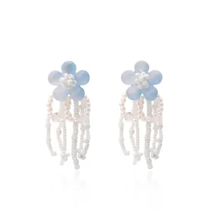 Close-up of light blue flower earrings with elegant white beaded tassels on white background