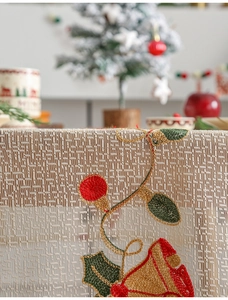 Detailed close-up of Christmas embroidery with bells and holly on beige woven tablecloth