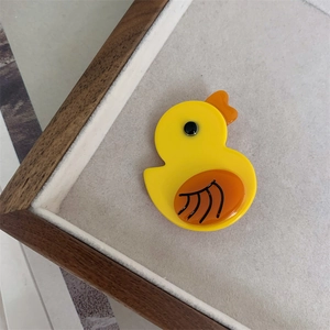 Detail shot of a yellow acetate duck hair clip with orange beak on a beige felt display tray