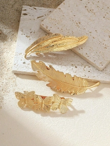 Detail view of gold metal hair clips in feather and butterfly designs on stone background