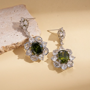 Close-up of silver oval green zircon earrings with flower-shaped crystal halo