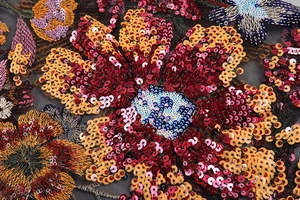 Macro detail of colorful floral and butterfly sequin embroidery on black mesh fabric