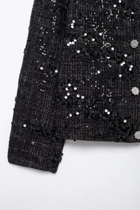 Detail der schwarzen Tweedjacke mit schimmernden Pailletten und glitzerndem Kristallknopf