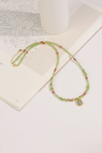 Macro view of beaded necklace with green peridot, pink tourmaline and golden square pendant