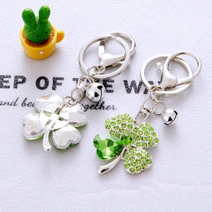Detail of silver clover keychain with green crystals and small bell on a decorative setup