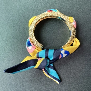 Close-up of matte gold textured cuff bracelet tied with a vibrant patterned silk scarf