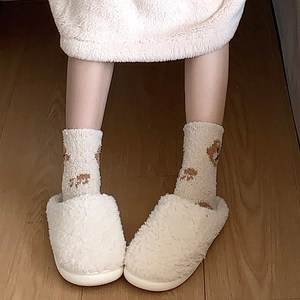 Close-up of fluffy coral fleece bear paw socks with plush cream slippers on wooden floor