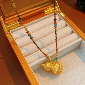 Macro shot of gold hollow gourd pendant and multicolored beaded necklace in a wood box