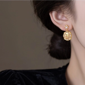 Close-up of gold flower earring with pearl and ginkgo leaf relief on velvet backdrop