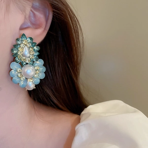 Close-up of vintage floral stud earrings with blue rhinestones and pearls on a model