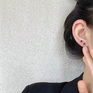 Pair of minimalist black zircon screw back earrings on a female ear with a grey background