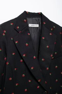 Détail de la broderie fraise sur un blazer noir avec étiquette de taille visible