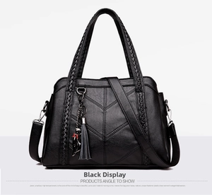 Detail view of black pebbled leather handbag with V-shaped stitching and cat charm