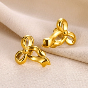 Detailed close-up of golden bow-shaped stud earrings on light beige silk background