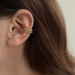 Detail of layered gold ear cuff with pearls and single diamond stud on ear