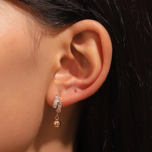Close-up of golden geometric earrings with rectangular zircons and a smooth metallic ball
