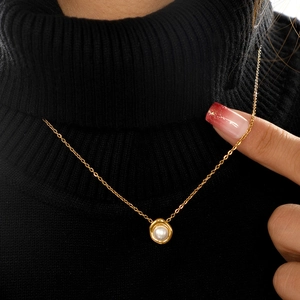 Detail of round white pearl pendant with gold plating worn on black knitwear