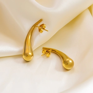 Macro detail of golden hollow teardrop earrings on elegant beige silk fabric background
