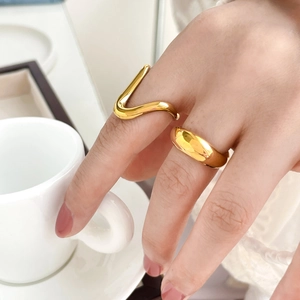 Detail of minimalist wavy and thick gold-plated rings on hand holding a white coffee cup