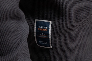 Macro detail of dark grey waffle knit fabric with a blue decorative fashion label