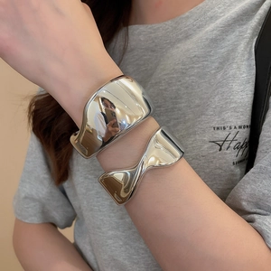 Detail of chunky silver horseshoe buckle bangle and wrinkled metal bracelet on wrist