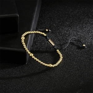 Detail of adjustable black woven bracelet with gold-plated copper beads on black textured surface