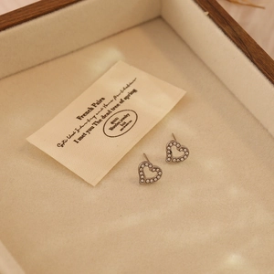 Macro shot of silver heart-shaped diamond stud earrings in a wooden jewelry box