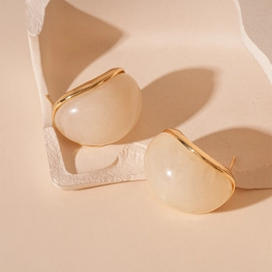 Detail shot of vintage beige resin stud earrings with gold metal trim on minimalist stone