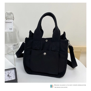 Detailed view of a black canvas tote bag with adjustable strap and front snap pocket