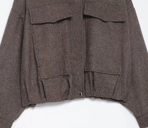 Detail shot of brown herringbone bomber jacket featuring large cargo pockets and texture
