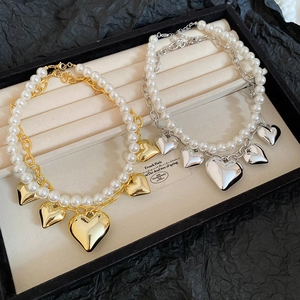 Close-up of gold and silver heart necklaces with layered pearls in a black box