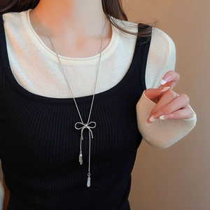 Close-up of a silver bowknot pendant necklace with tassels on a model's neck