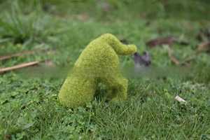 Detail showing the grass-like texture of a green flocked puppy garden ornament outdoors