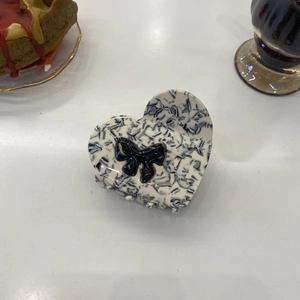 Detail of heart acetate claw clip with marble pattern and elegant black bow hair accessory