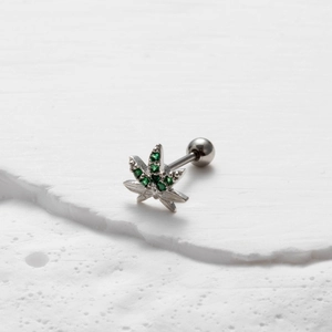 Macro shot of silver hemp leaf ear stud with green gemstones on white stone surface