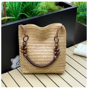 Detail of straw woven bucket bag with beaded wooden handle on a wooden table