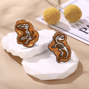 Detailed enamel pins featuring dinosaur fossil skeletons on warm minimalist background