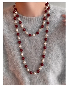 Dettaglio della collana di perline rosse e perle su un maglione grigio lavorato a maglia