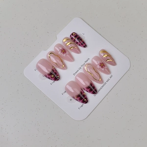 Macro shot of long almond press-on nails with pink flowers and gold embossed details