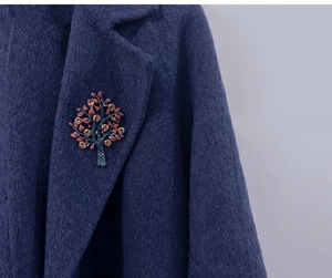 Detail view of crystal tree brooch with red and amber stones on navy wool coat