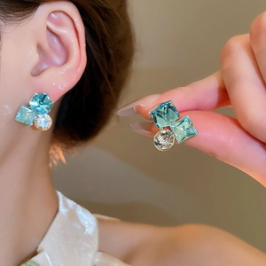 Close-up of geometric 18k gold plated earrings with blue square crystal and zircon studs