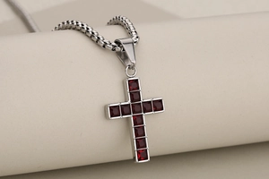 Detail shot of silver cross pendant with red gemstones on a box chain necklace